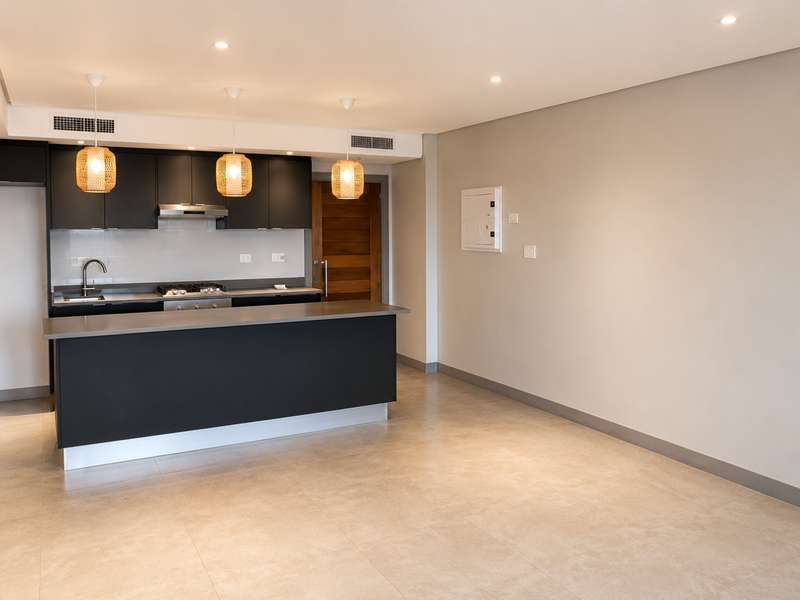 Modern open-plan kitchen featuring sleek dark cabinetry, stone countertops, integrated gas hob, and neutral tiled flooring in a spacious, well-lit living area.