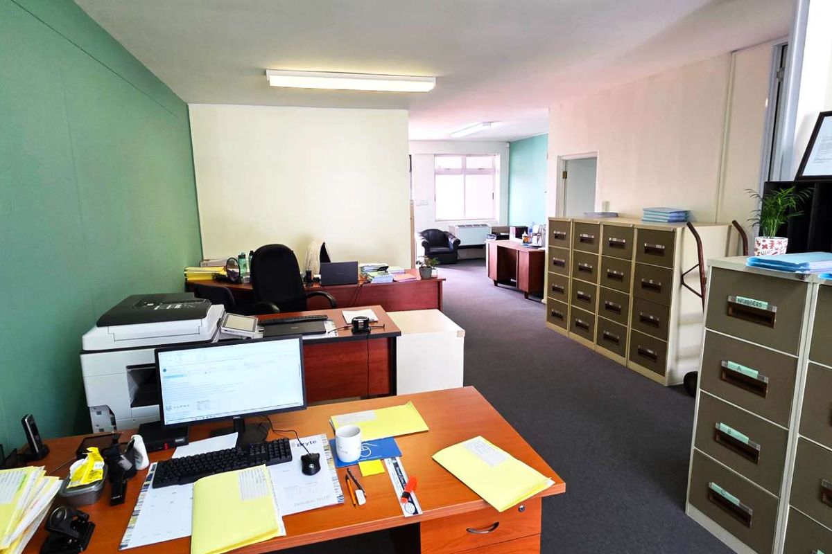 A functional office space featuring carpeted flooring, fluorescent lighting, and partition walls, providing a practical layout for a professional work environment.