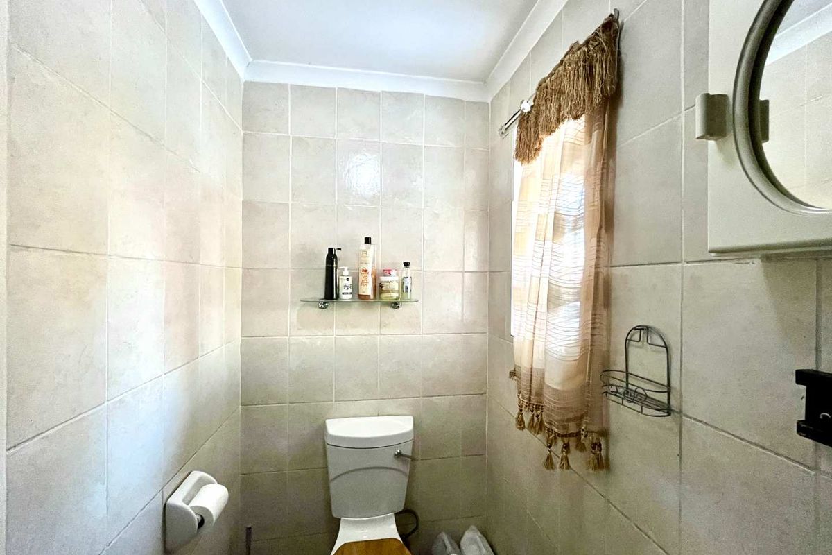 A compact bathroom featuring full-height wall tiling, a standard toilet, and built-in storage fixtures, offering a functional space with potential for modern updates.