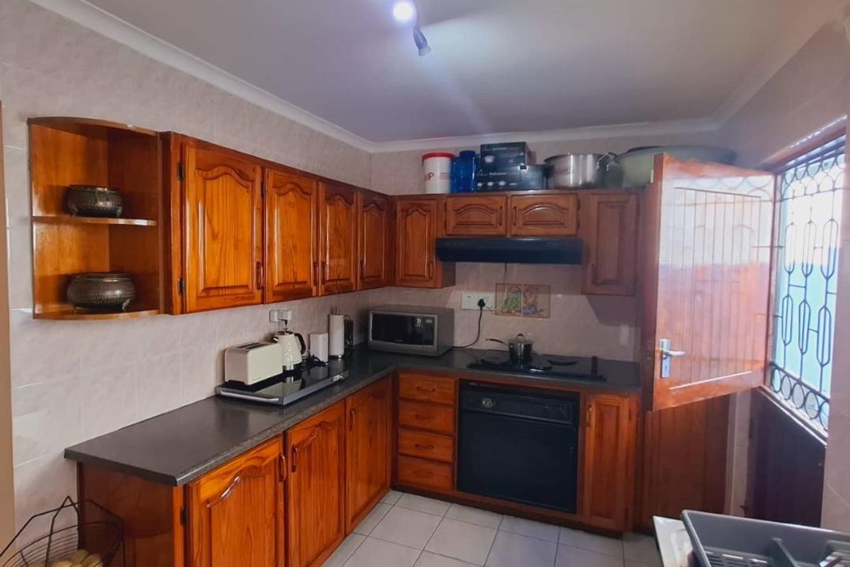 A functional kitchen featuring traditional wooden cabinetry, dark countertops, built-in oven and hob, and tiled flooring with direct access to the exterior.