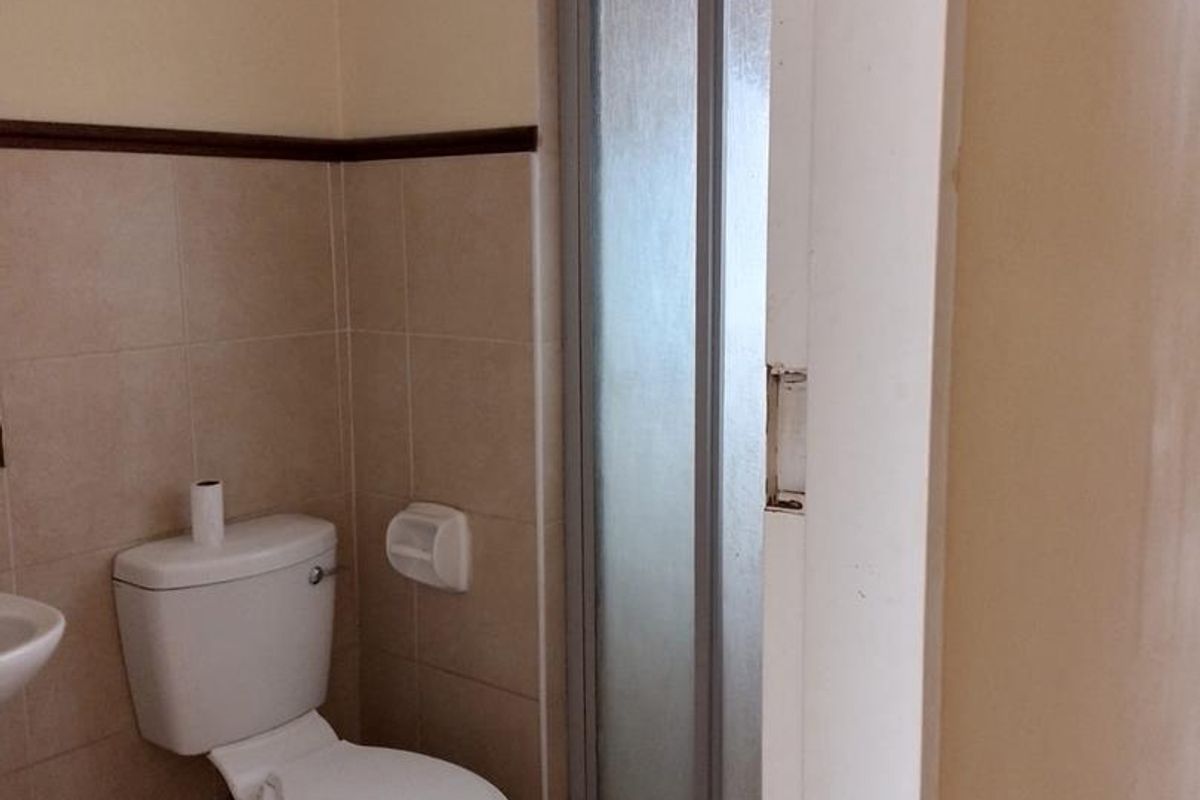A compact bathroom featuring a toilet, basin, and a shower enclosure with a sliding door, finished with neutral wall and floor tiles.