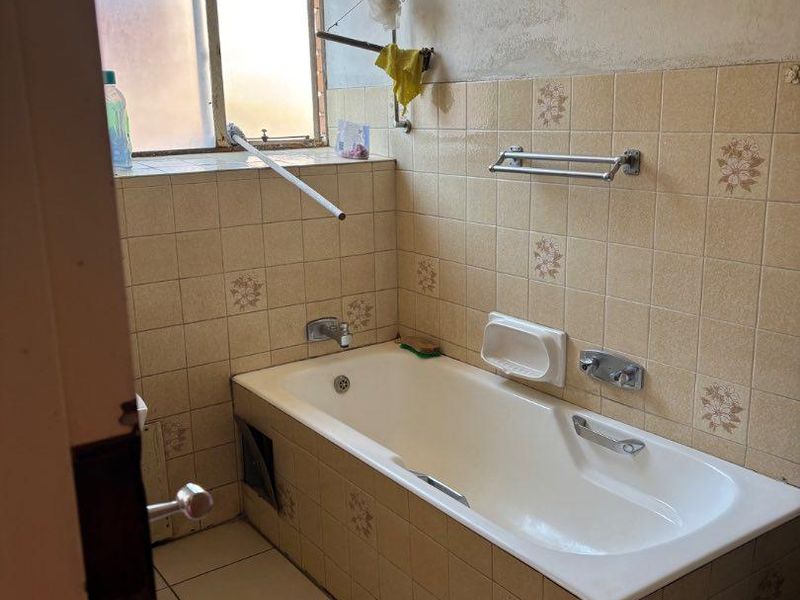 A dated bathroom featuring a built-in bathtub with tiled surround, requiring renovation to update the finishes and fixtures.