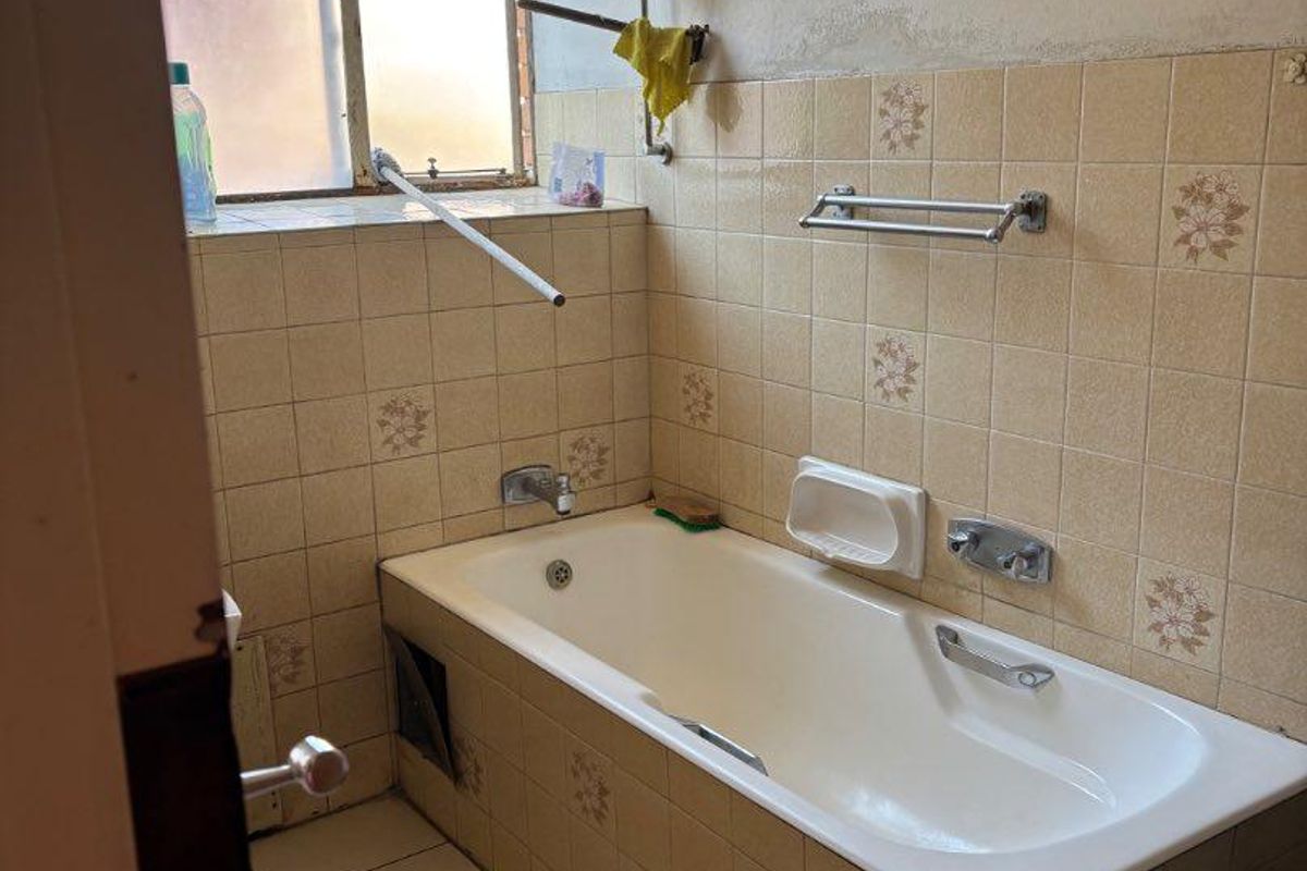 A dated bathroom featuring a built-in bathtub with tiled surround, requiring renovation to update the finishes and fixtures.