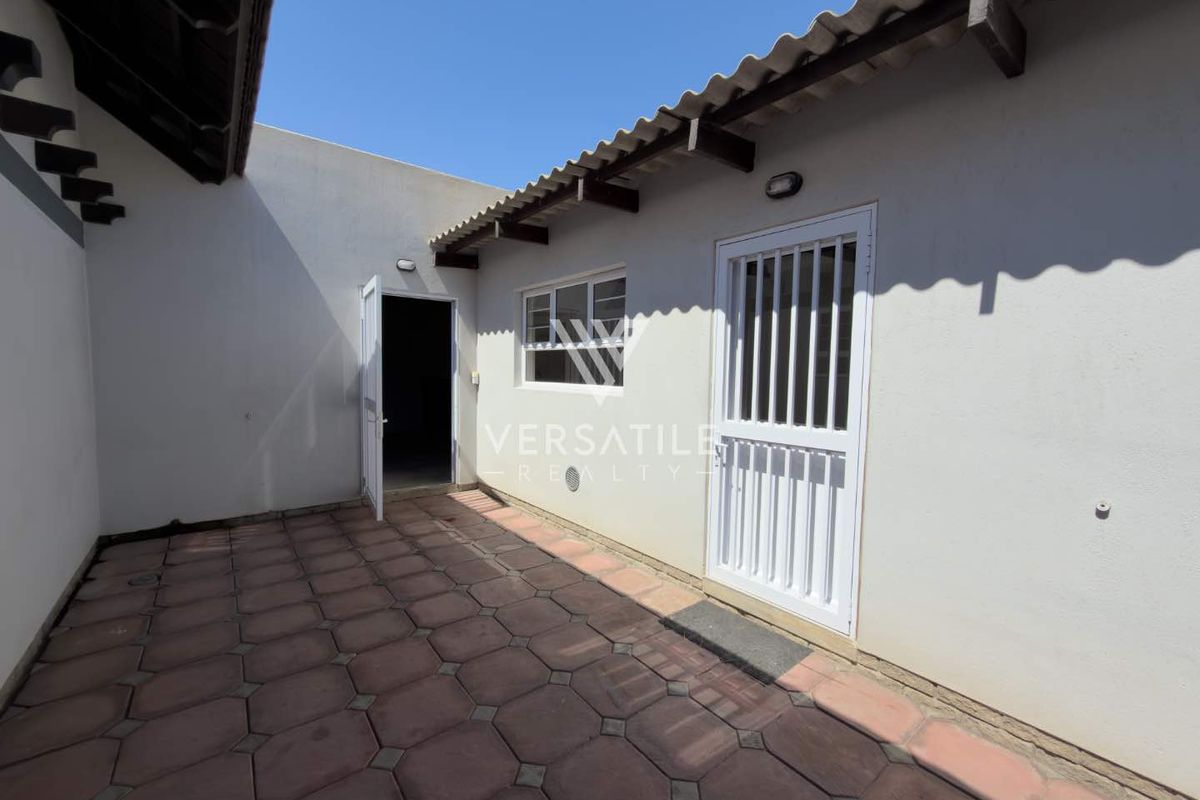 A paved rear courtyard area featuring exposed timber rafters, a security gate, and direct access to the home's interior.