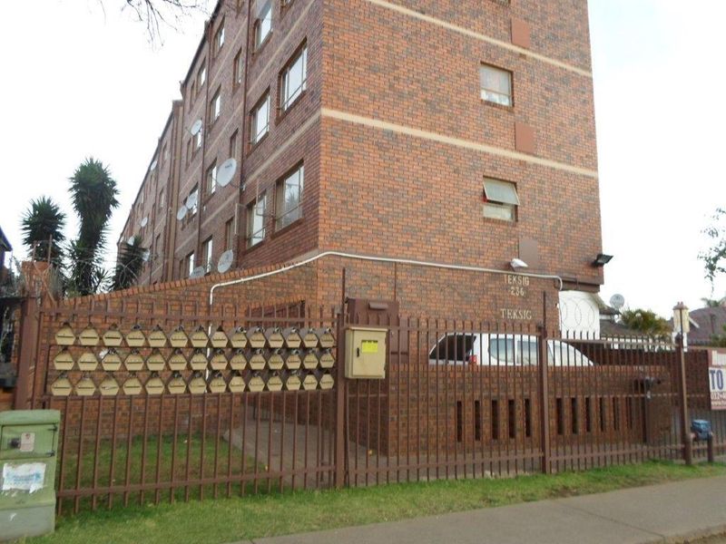 Exterior view of a multi-story face brick apartment building featuring perimeter security fencing and a bank of mailboxes.