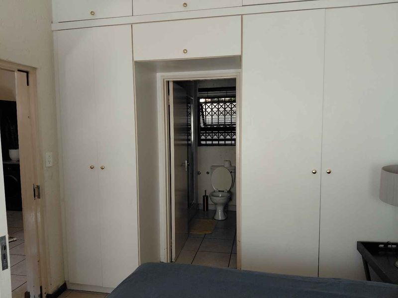Bedroom featuring extensive built-in cupboards and direct access to an en-suite bathroom with tiled flooring.
