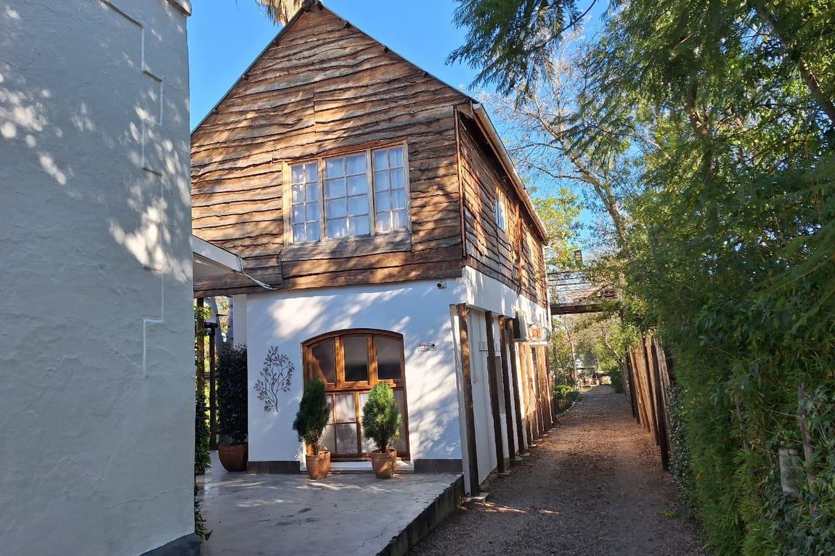 Exterior view of a two-story building featuring a rustic timber-clad upper level and a white-rendered ground floor with arched wooden door and windows.