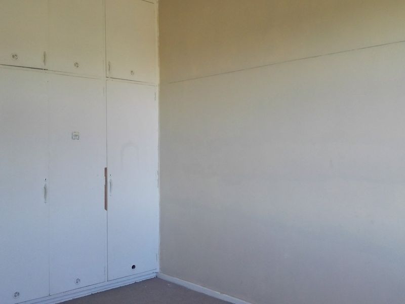 An empty bedroom featuring built-in cupboards with some visible wear and a missing handle, offering a blank canvas for renovation.