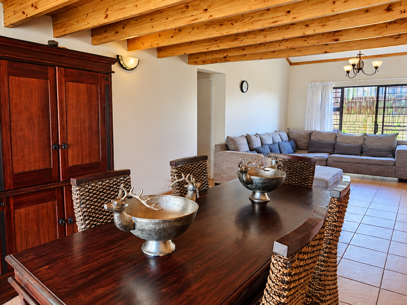 Spacious open-plan living and dining area featuring exposed timber ceiling beams, ceramic floor tiles, and a staircase leading to the upper level.