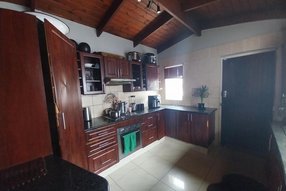 Kitchen featuring dark wood cabinetry, granite countertops, built-in oven, and exposed timber ceiling beams with tiled flooring.