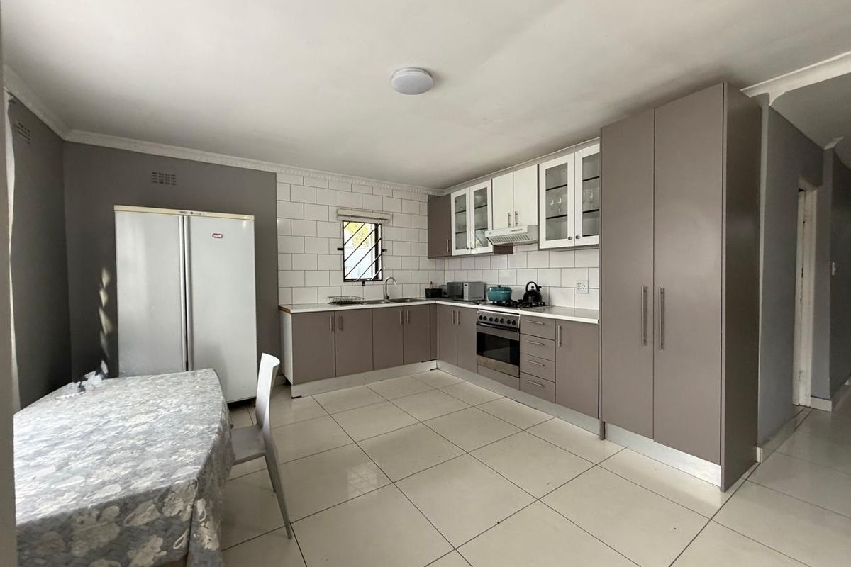 A functional kitchen featuring modern cabinetry, tiled splashbacks, a built-in oven with extractor fan, and tiled flooring in an open-plan layout.