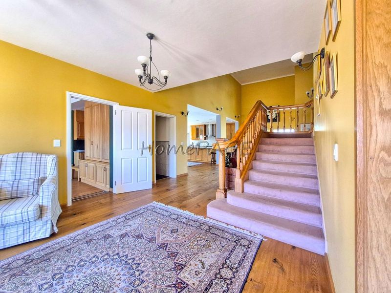 Spacious entrance hall featuring hardwood flooring, a timber staircase with a classic balustrade, and direct access to adjoining living and kitchen areas.