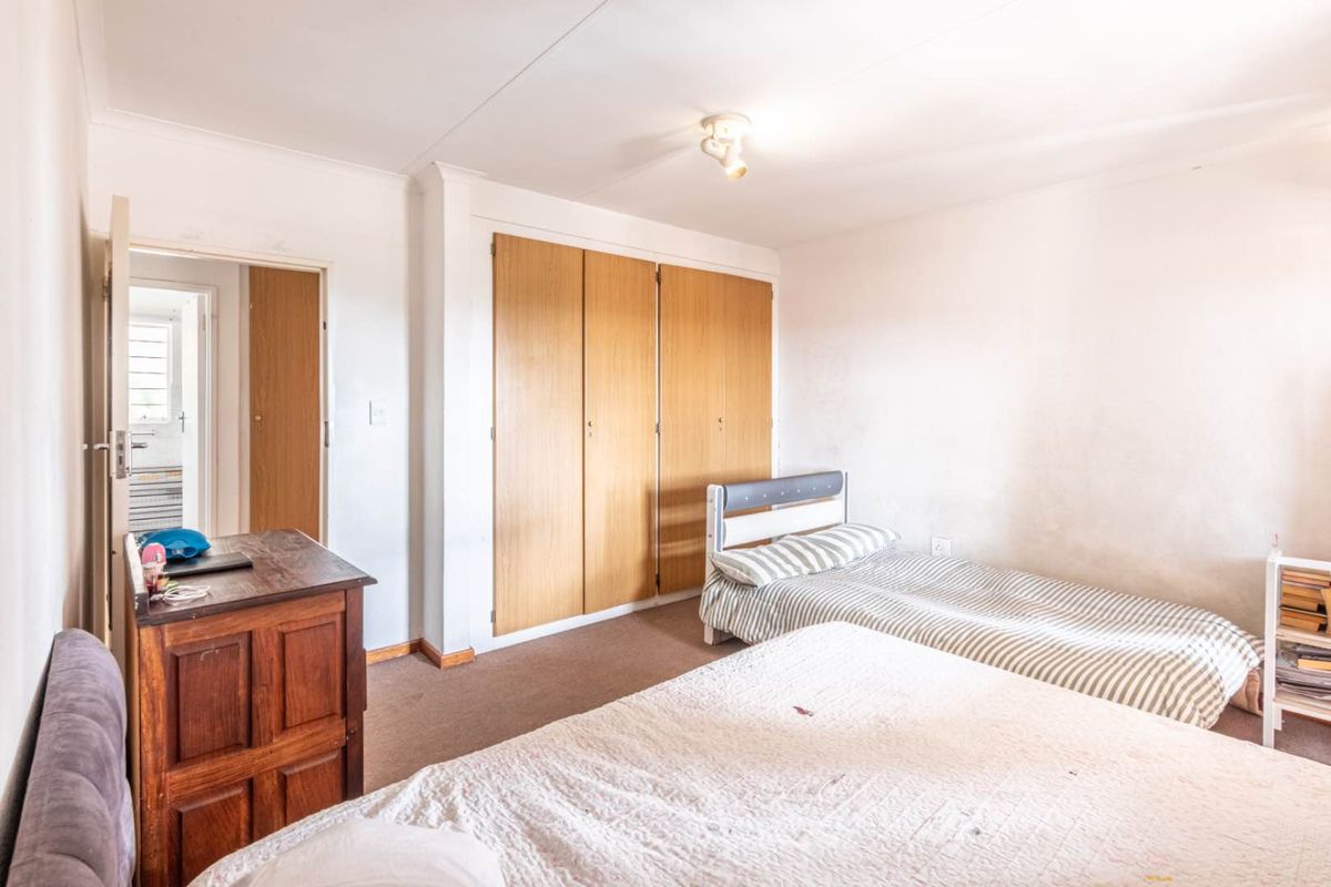 A bedroom featuring built-in wooden cabinetry, carpeted flooring, and access to an adjacent room, offering a functional space with potential for cosmetic updates.
