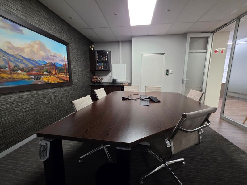 A professional boardroom featuring a dark wood conference table, textured feature wall, suspended ceiling, and glass partition wall for a modern office environment.