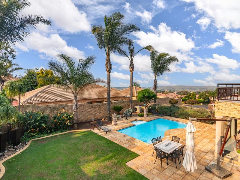 A well-maintained outdoor pool area featuring a paved patio, landscaped garden, and a swimming pool, set against a backdrop of residential views.