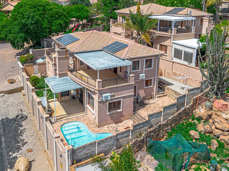 Aerial view of a multi-story residential property featuring a tiled roof with solar panels, a swimming pool, and a spacious balcony.