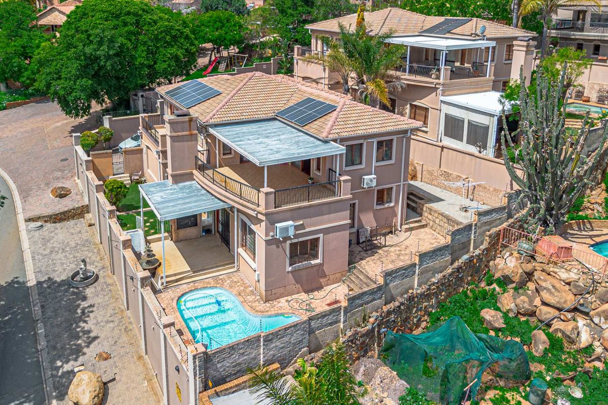 Aerial view of a multi-story residential property featuring a tiled roof with solar panels, a swimming pool, and a spacious balcony.