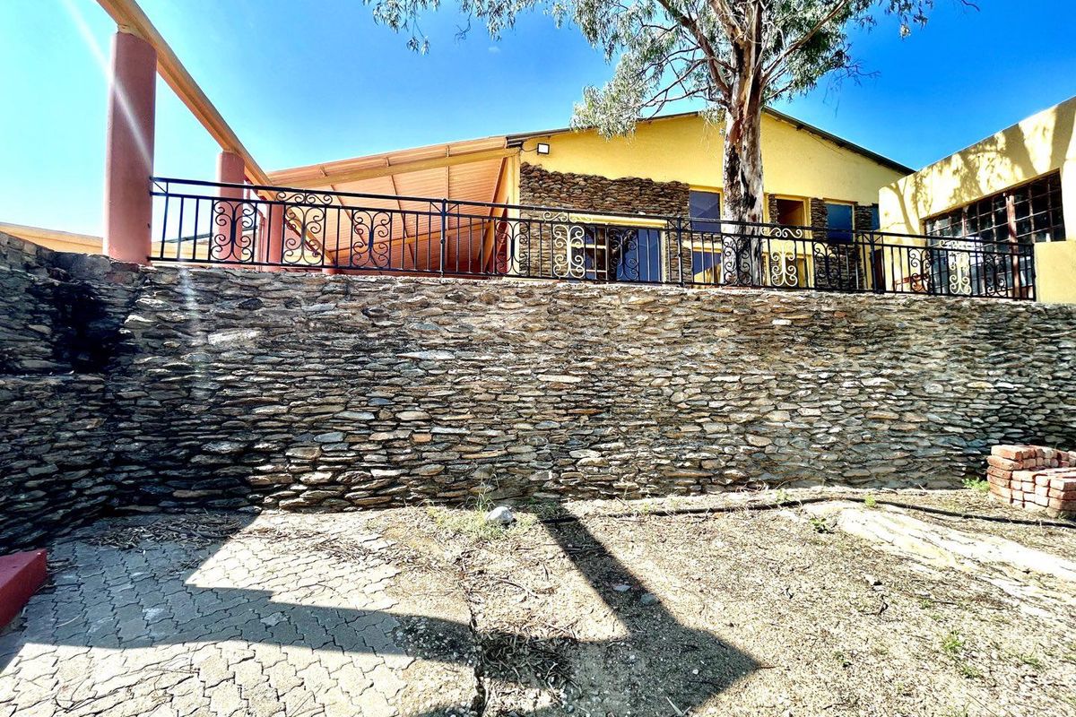 Rear exterior view featuring a stone retaining wall, paved ground area, and a raised patio with wrought iron railings.