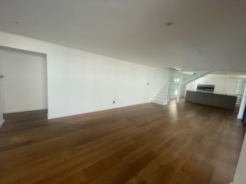 Spacious open-plan living area featuring hardwood flooring, recessed lighting, a modern staircase with glass balustrade, and a sleek kitchen with built-in cabinetry.