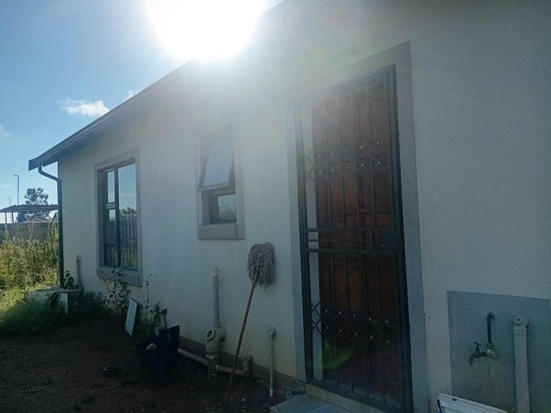 Rear exterior view of the property featuring a security gate, external water tap, and plumbing infrastructure against a plastered wall.