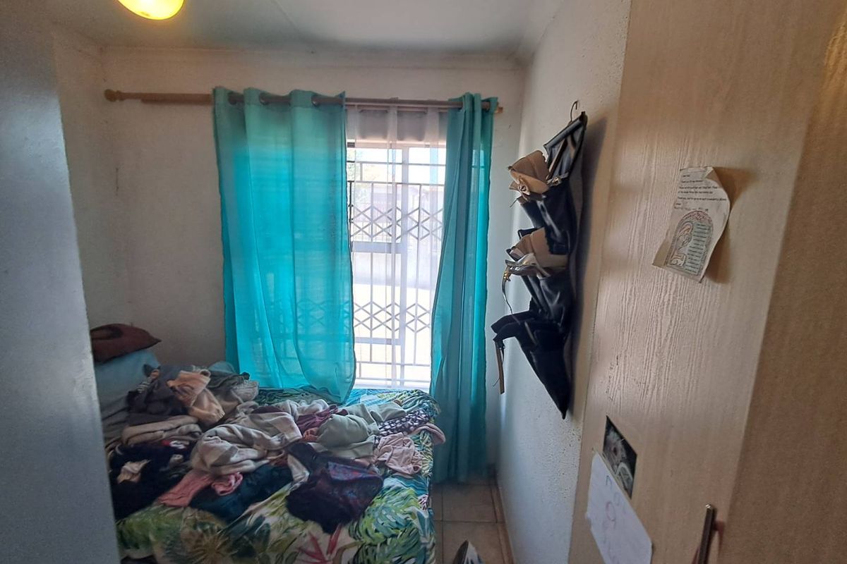 A compact bedroom featuring a window with security bars and built-in wooden cabinetry.