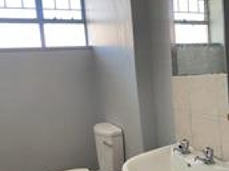 A functional bathroom featuring a pedestal basin, toilet, and tiled flooring, with a window providing natural light.