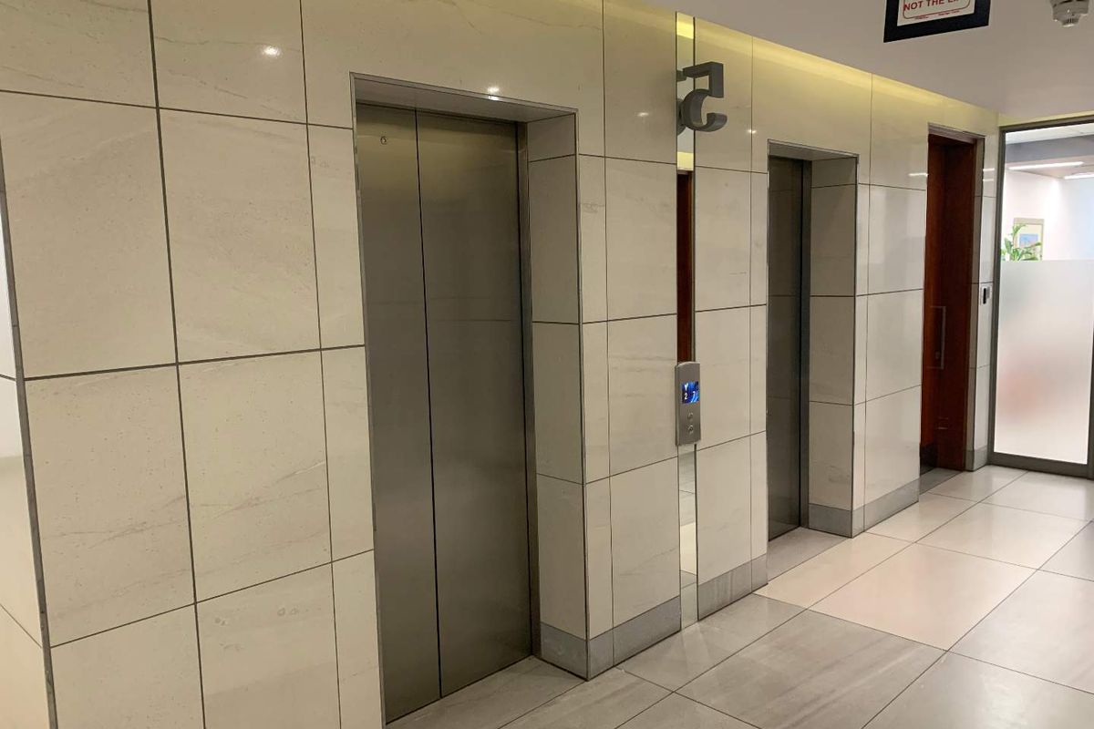 A modern office building elevator lobby featuring stainless steel lift doors, polished tiled flooring, and contemporary wall tiling.