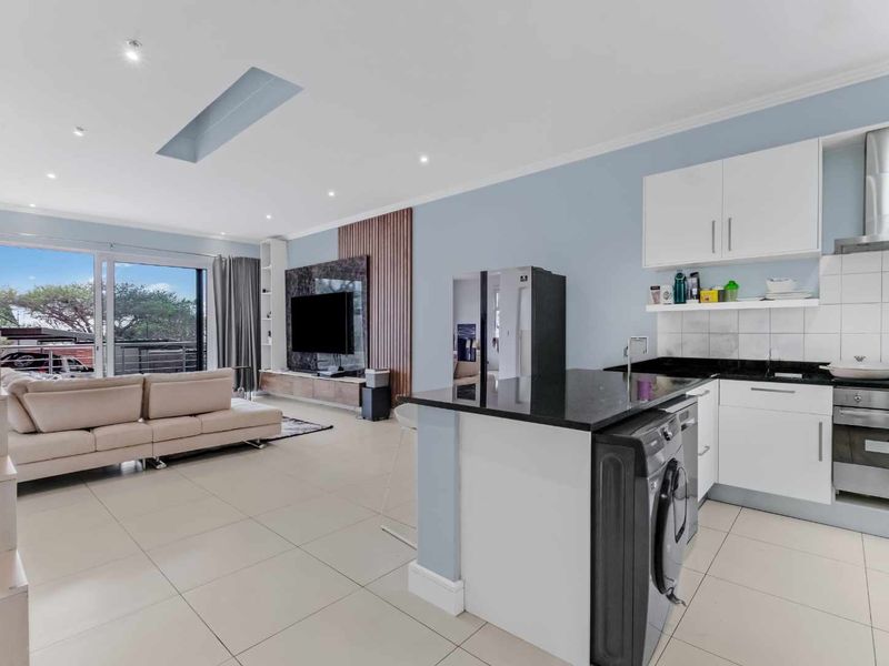 Modern open-plan living area featuring a sleek kitchen with granite countertops, built-in appliances, tiled floors, and seamless access to a balcony through sliding doors.