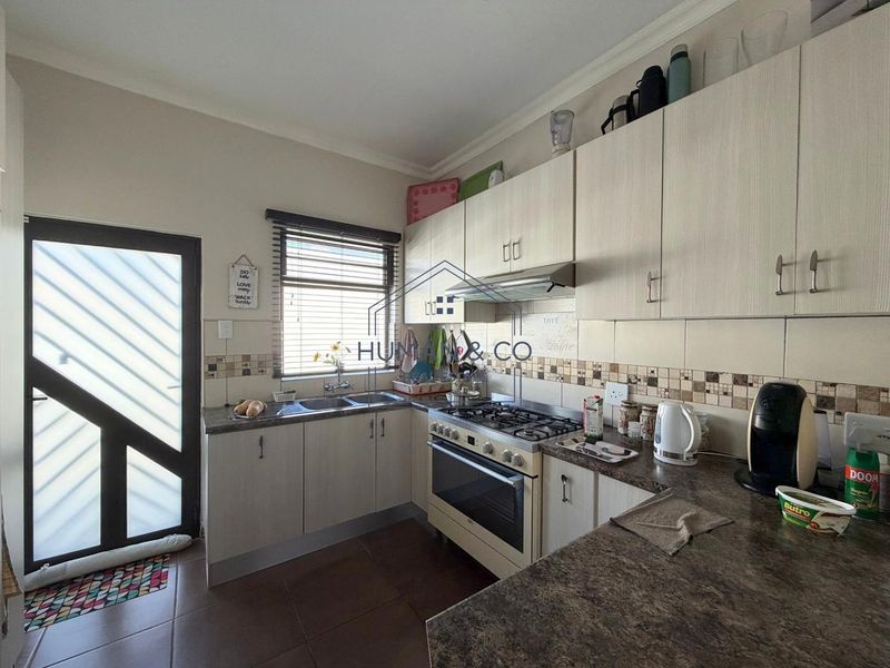 A functional kitchen featuring light-toned built-in cabinetry, gas stove with extractor, double basin sink, and tiled finishes with direct access to the exterior.