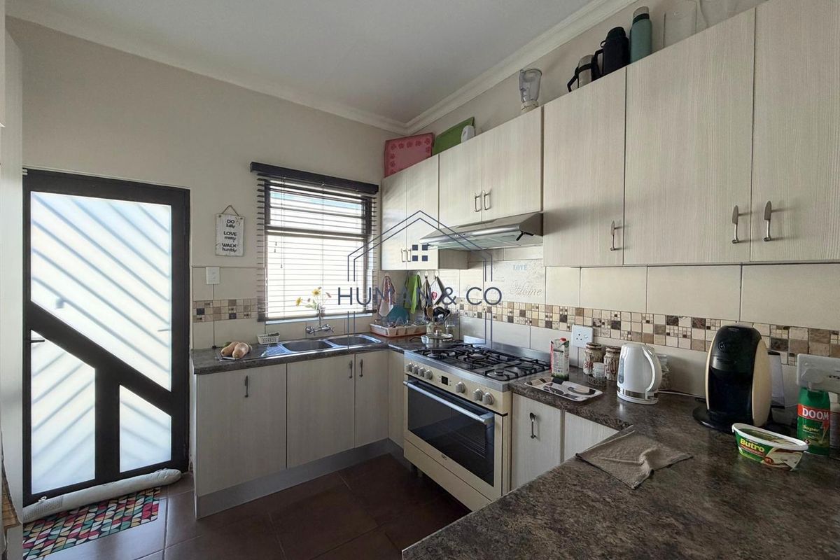 A functional kitchen featuring light-toned built-in cabinetry, gas stove with extractor, double basin sink, and tiled finishes with direct access to the exterior.