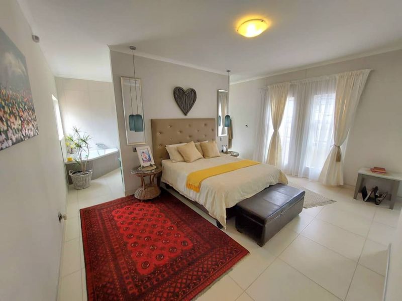 Spacious bedroom featuring tiled flooring, neutral walls, and an open-plan en-suite bathroom area with a built-in corner bathtub.