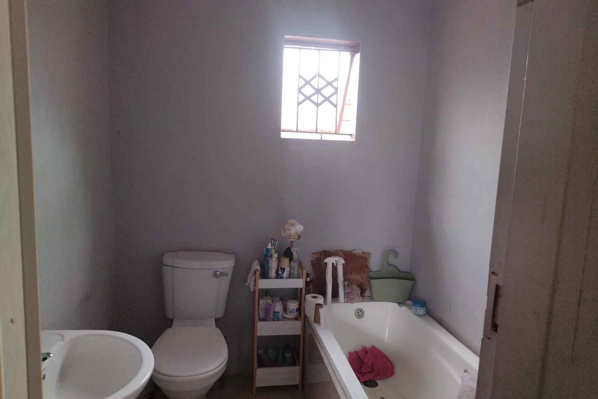 A compact bathroom featuring a standard bathtub, toilet, and pedestal basin with a small window providing natural light.