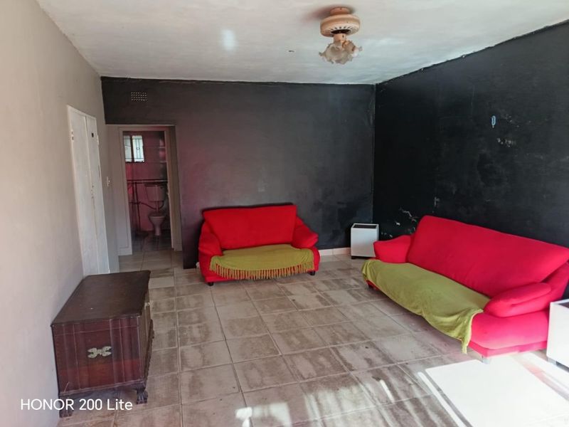 A living room area featuring tiled flooring and a ceiling fan, with visible wear on the wall finishes.