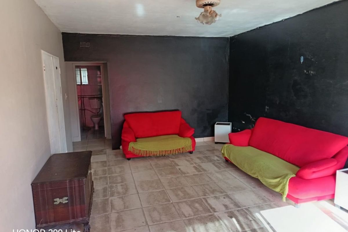 A living room area featuring tiled flooring and a ceiling fan, with visible wear on the wall finishes.