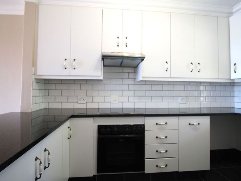 A clean, modern kitchen featuring white cabinetry, black granite countertops, a subway tile backsplash, and integrated appliances including an oven and extractor fan.