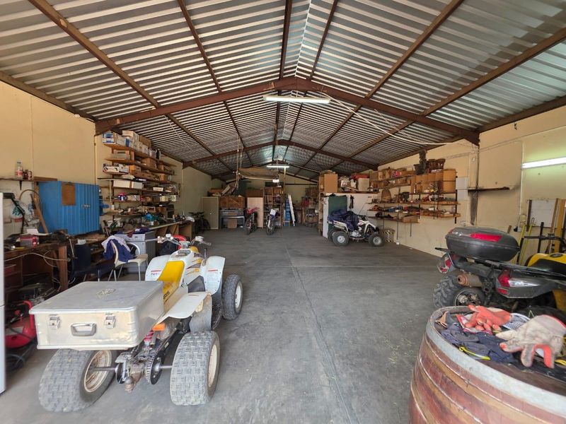 A spacious, functional garage featuring a high-pitched metal roof, exposed steel trusses, concrete flooring, and extensive built-in wall shelving for storage.