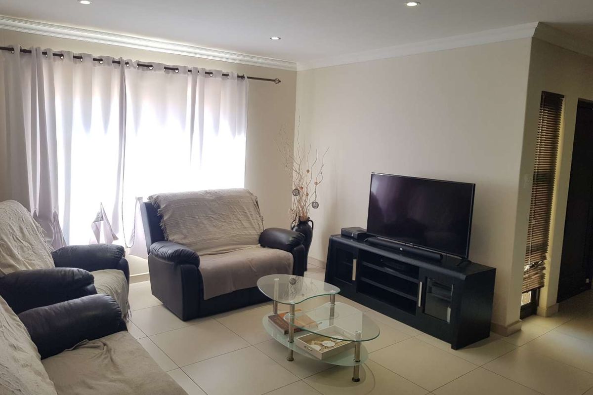 A bright living room featuring neutral tiled flooring, recessed ceiling lighting, and large windows with curtain tracks.