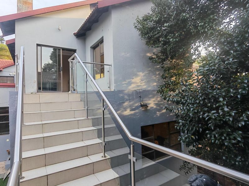 An exterior view of the rear of the house featuring a tiled staircase with a modern stainless steel and glass balustrade leading to a sliding door.