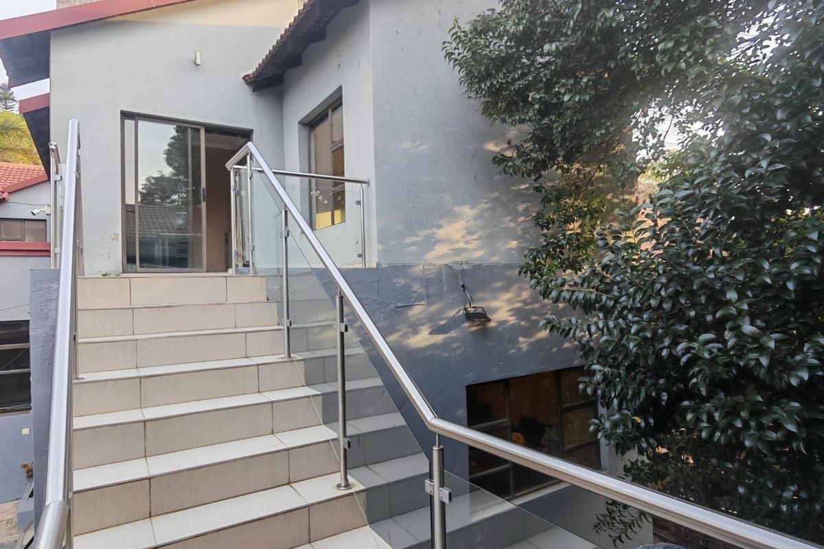An exterior view of the rear of the house featuring a tiled staircase with a modern stainless steel and glass balustrade leading to a sliding door.