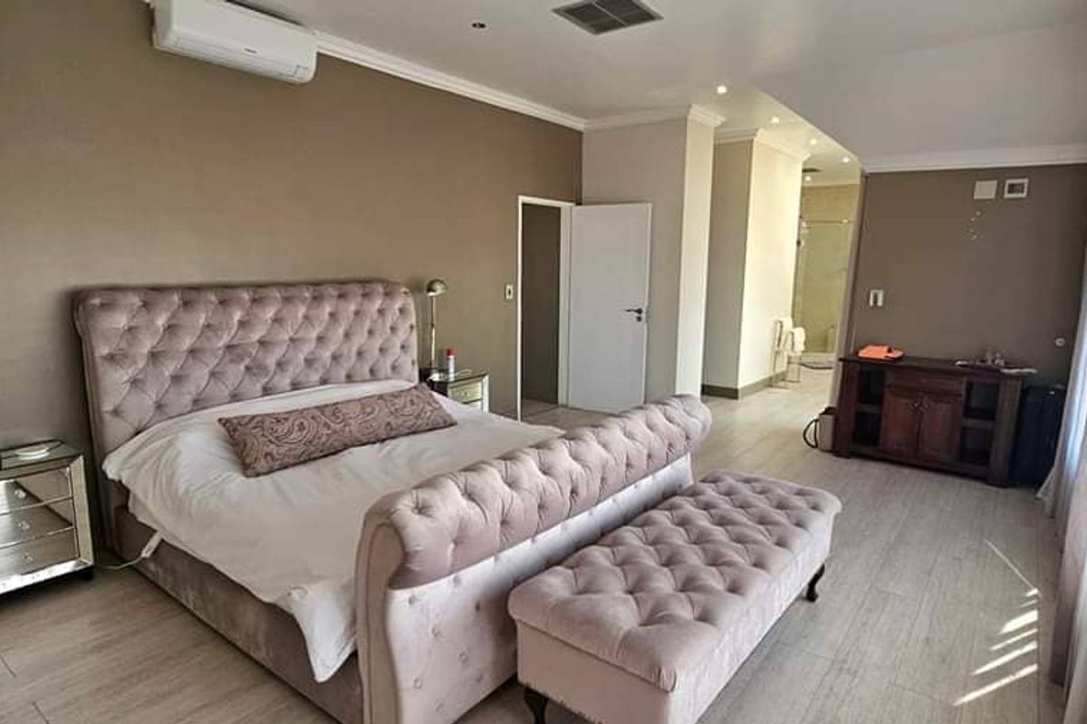 Spacious bedroom featuring wood-look flooring, crown molding, a wall-mounted air conditioning unit, and an en-suite bathroom area.