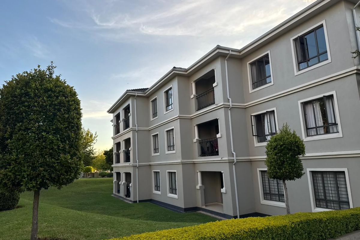 Exterior view of a multi-story apartment complex featuring grey facade, private balconies, and well-maintained landscaped garden areas.
