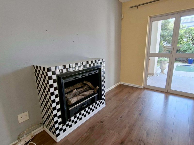 Living room featuring a built-in fireplace with checkered tile surround, laminate flooring, and direct access to the patio through a glass sliding door.