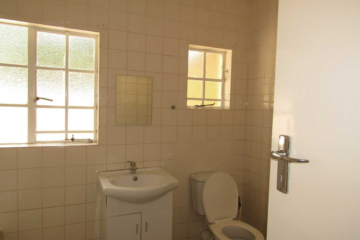 A dated bathroom featuring wall-to-wall tiling, a pedestal vanity, and a standard toilet, requiring cosmetic updates to modernize the space.