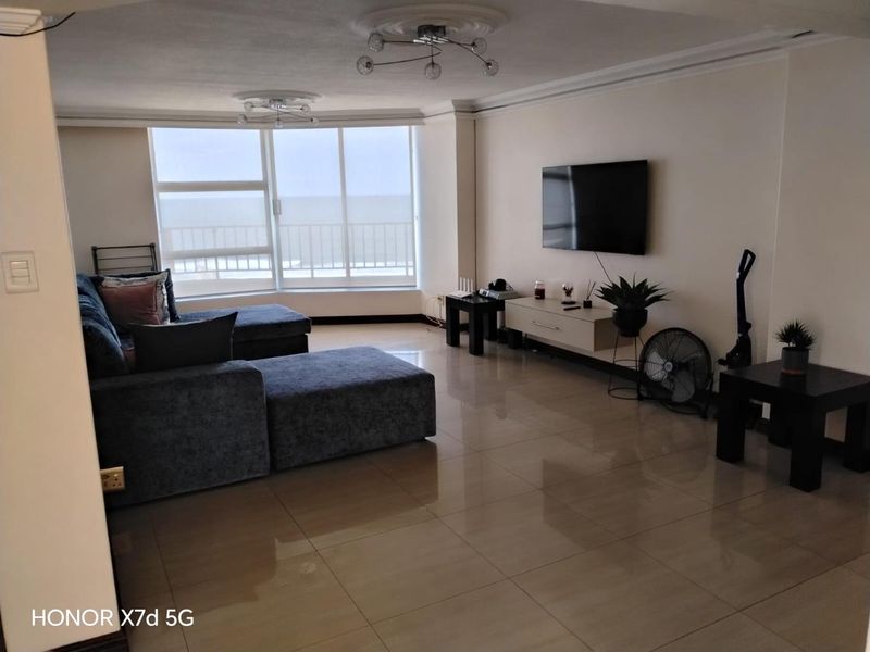 Spacious living room featuring large sliding glass doors with ocean views, polished tile flooring, and decorative ceiling roses.
