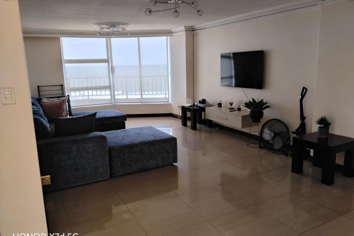 Spacious living room featuring large sliding glass doors with ocean views, polished tile flooring, and decorative ceiling roses.