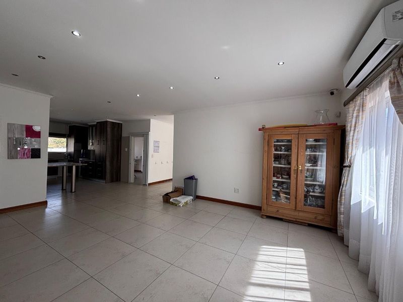Spacious open-plan living area featuring neutral tiled flooring, recessed downlighting, and a wall-mounted air conditioning unit, with a seamless flow to the kitchen.