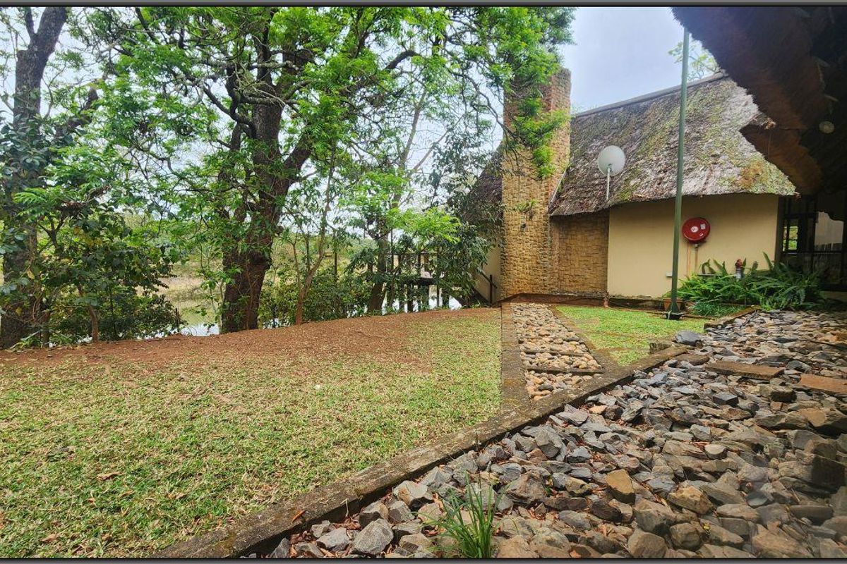 Rear garden view featuring a thatched roof dwelling with stone chimney, stone cladding, and a landscaped stone pathway leading to the lawn.