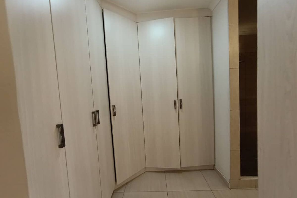 A clean, functional dressing area or bedroom space featuring light-toned built-in cupboards and neutral floor tiles.
