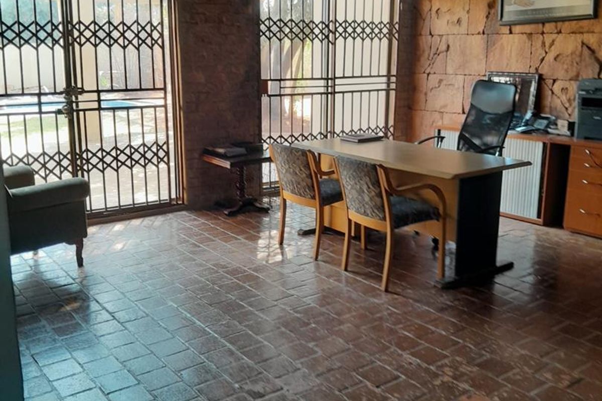 A rustic home office featuring exposed brick walls, terracotta tile flooring, and large sliding glass doors with security gates leading to the exterior.