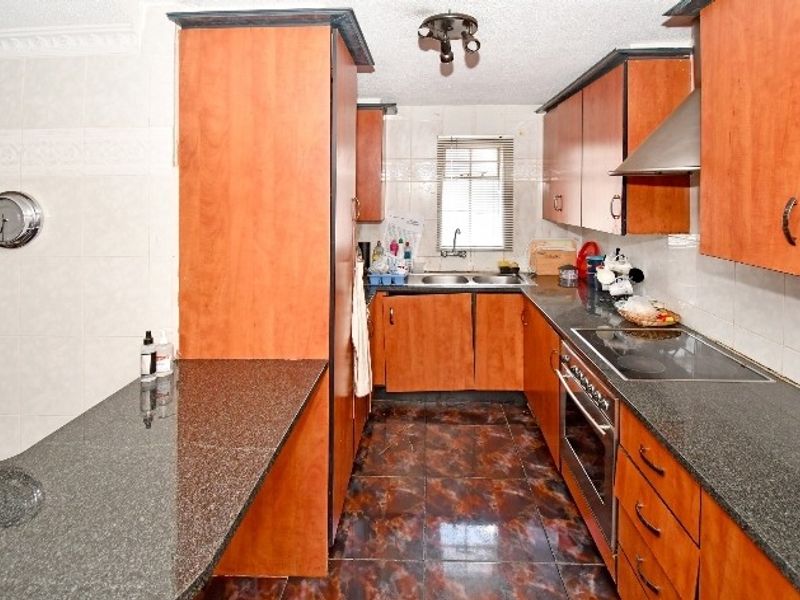 A functional kitchen featuring wood-finish cabinetry, granite countertops, integrated oven and hob, and tiled flooring with a practical layout.